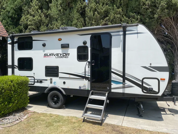 This white Surveyor Legend travel trailer with extended steps is ideal for an RV rental. It's parked on concrete.. Forest River Surveyor Legend 2023