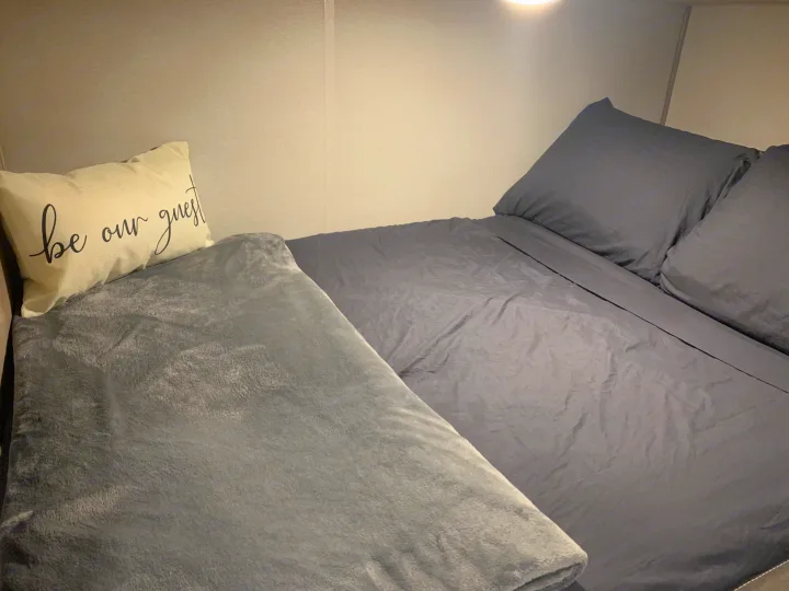 Cozy RV rental bedroom with two beds, soft blankets, and a welcoming "be our guest" pillow.. Forest River Aurora Aurora Light 2024