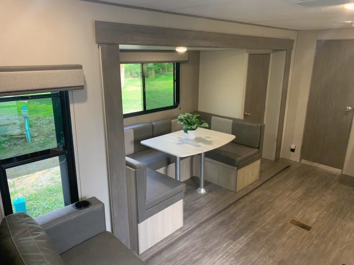 Modern RV rental interior: A bright dining area with cozy bench seating, a white table, and a large window view.. Forest River Aurora Aurora Light 2024