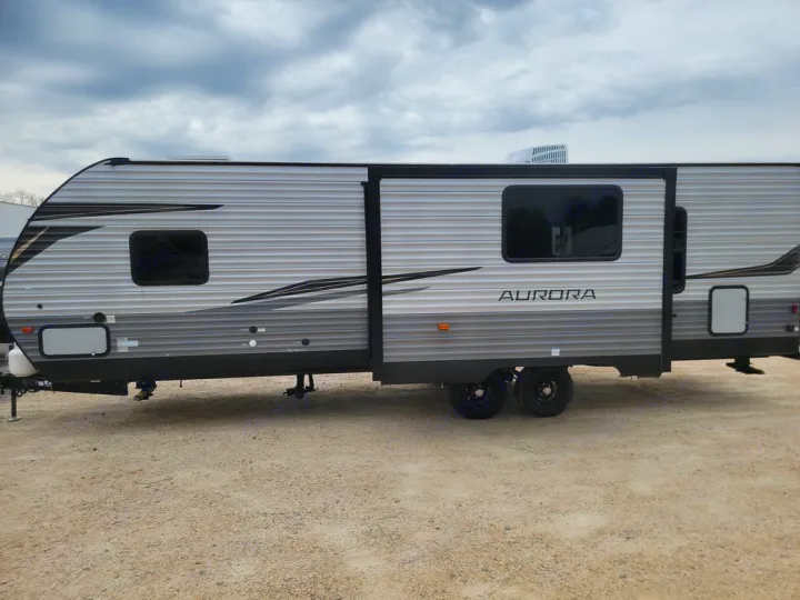 Grey and black Aurora travel trailer for RV rental, parked on gravel under a cloudy sky.. Forest River Aurora Aurora Light 2024