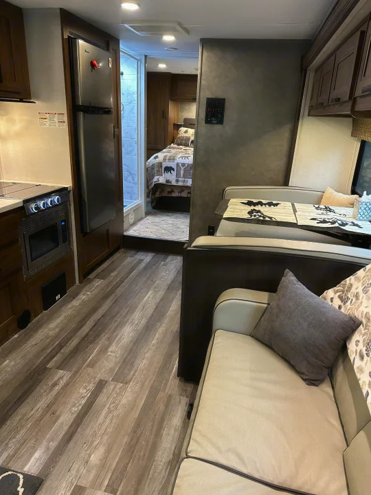 RV rental interior: a modern kitchen, comfortable dining area, and a cozy bedroom with warm, rustic bedding. Wood-look flooring.. Forest River Sunseeker LE 2021
