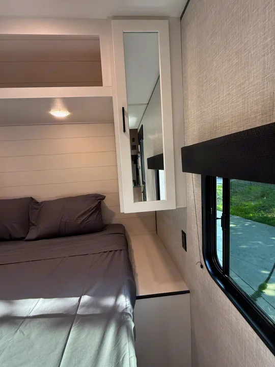 Cozy RV rental bedroom with a gray bed, mirrored cabinet, and a window, offering comfort for your travels.. Jayco Jay Flight 2025