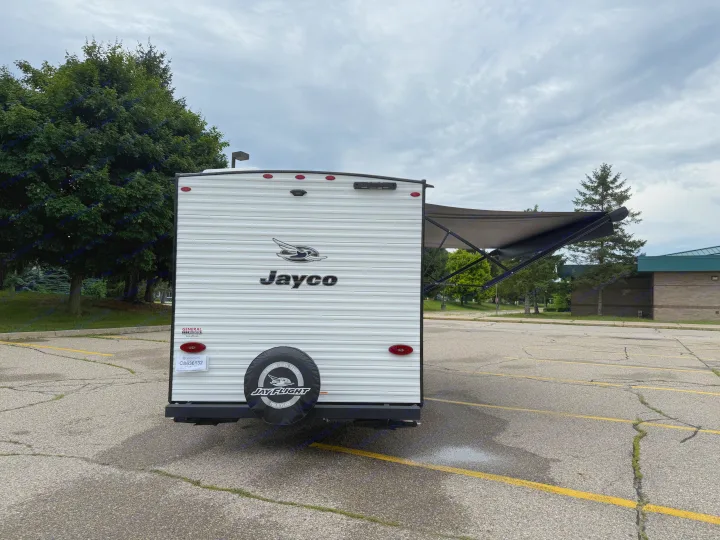 Rear view of a white Jayco travel trailer RV rental with an extended awning, parked in an asphalt lot.. Jayco Jay Flight 2025
