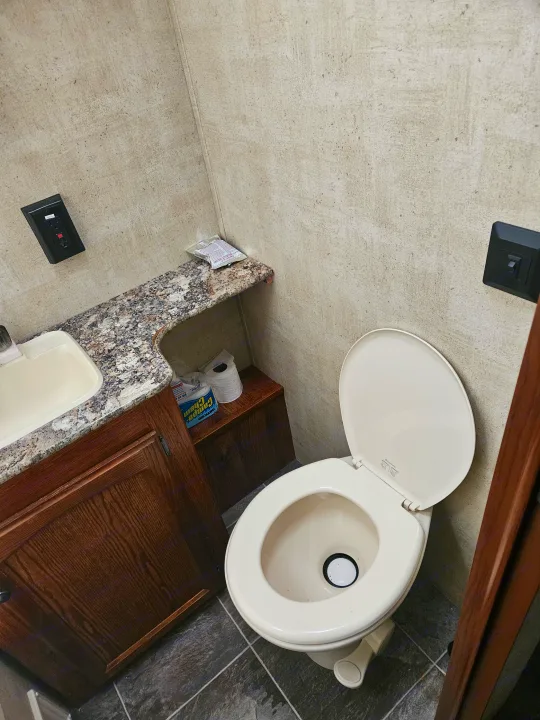 Compact RV rental bathroom with a beige toilet, sink, granite-style counter, and wood cabinets. Walls have light paneling.. Keystone RV Hideout 2015