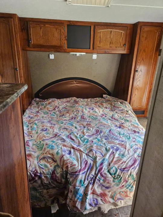 Cozy RV rental bedroom with a vibrant comforter, overhead cabinets, and side storage. Perfect for travel comfort.. Keystone RV Hideout 2015