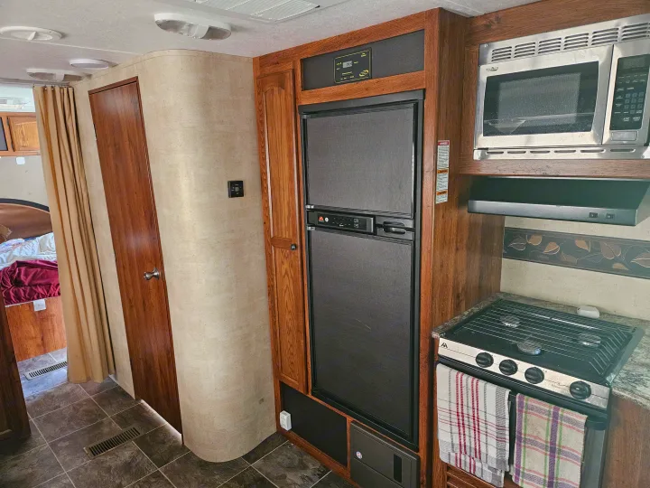 Compact RV rental interior featuring a full kitchen with microwave, fridge, stovetop, and a peek into the bedroom.. Keystone RV Hideout 2015