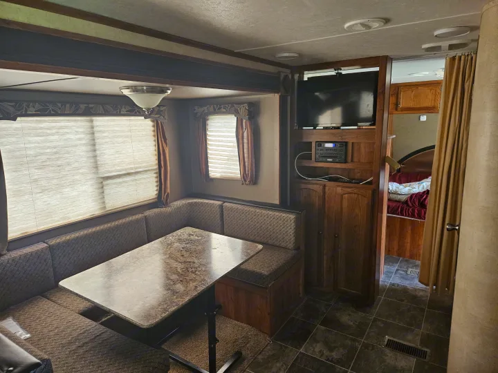 Spacious RV rental interior featuring a dinette, entertainment system, and access to a cozy bedroom.. Keystone RV Hideout 2015