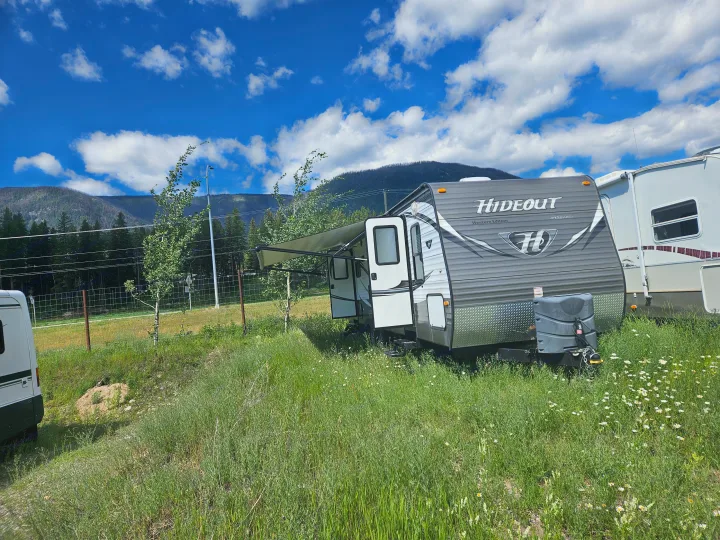 Hideout by Keystone travel trailer (RV rental) parked in a sunny, mountainous landscape with green grass and flowers.. Keystone RV Hideout 2015