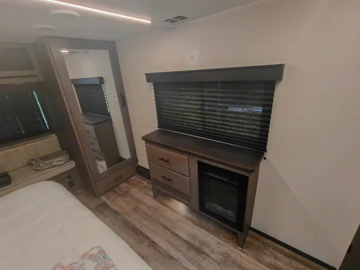 Comfortable RV rental interior: featuring a cozy bedroom with bed, mirrored wardrobe, and electric fireplace cabinetry.. Forest River Arctic Wolf 2025