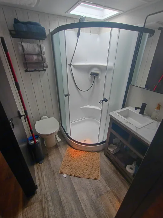 Modern and functional RV rental bathroom with a corner shower, toilet, sink vanity, and towel storage.. Forest River Arctic Wolf 2025