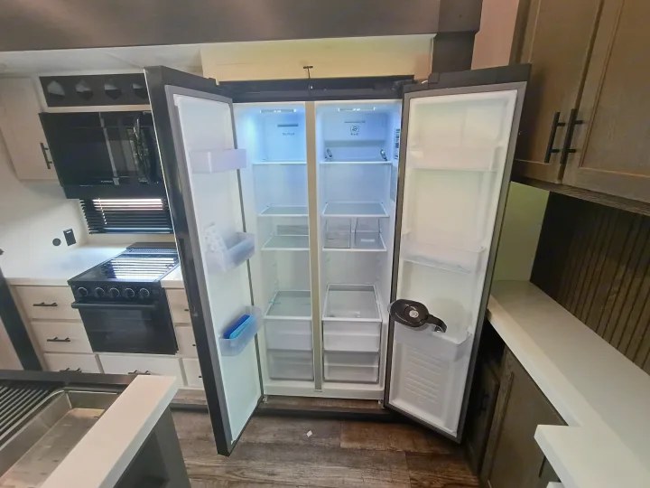 Bright & modern RV rental kitchen interior, featuring an open double-door refrigerator, stove, oven, and microwave.. Forest River Arctic Wolf 2025