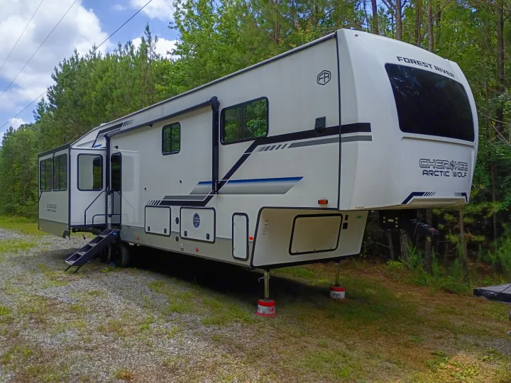 A large white fifth-wheel RV rental, a Forest River Cherokee Arctic Wolf, parked on gravel, set up for camping.. Forest River Arctic Wolf 2025