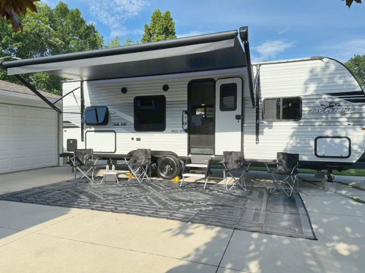 An RV rental, a Jay Flight travel trailer, is parked on a driveway with its awning extended, outdoor mat, and chairs set up.. Jayco Jay Flight 2025