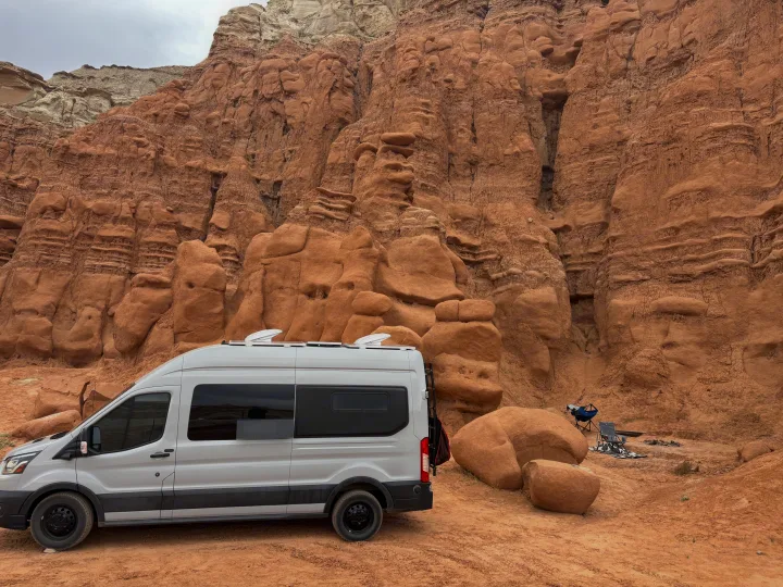 White RV rental camper van parked at a unique desert campsite amidst stunning red rock formations.. Ford Transit 2022