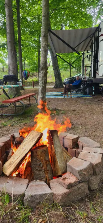 A perfect RV rental campsite setup: a glowing campfire, a person relaxing by their RV with a dog.. Starcraft Autumn Ridge 2014