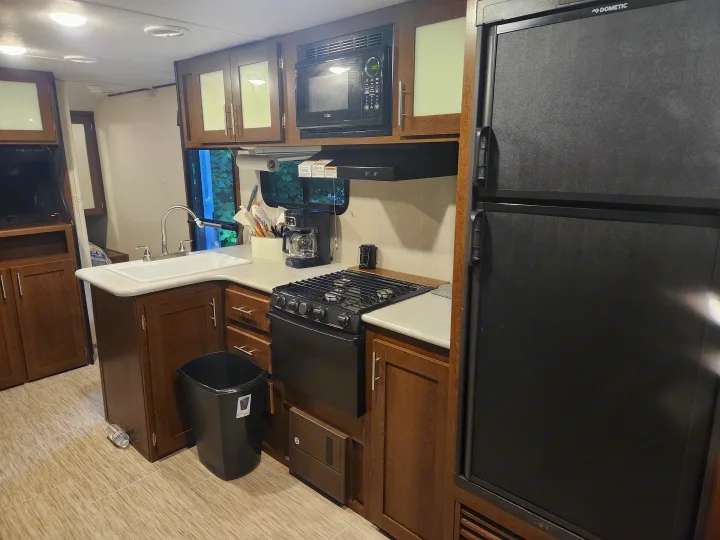 Explore this well-equipped RV rental kitchen featuring a sink, stove, microwave, and large refrigerator, perfect for travel adventures.. Forest River Acadia 2018