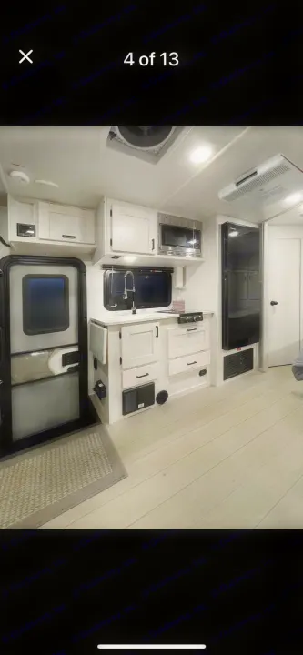 Bright, modern RV rental interior featuring a clean kitchen with white cabinets, microwave, fridge, and light wood-look floors.. east to west entrada 2023