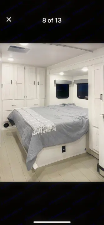 Bright RV rental bedroom features a comfy bed, ample white storage cabinets, and small windows, offering a cozy retreat.. east to west entrada 2023