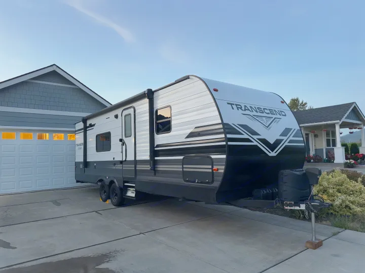 A large, modern Transcend travel trailer, perfect for an rv rental, parked on a home's concrete driveway.. Grand Design Transcend Xplor 2021