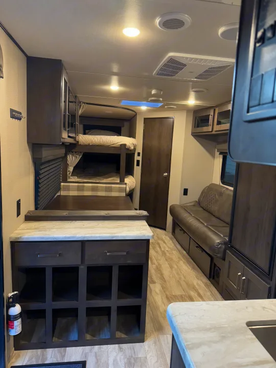 Inside an RV rental, showing bunk beds, a seating area, and a kitchen island.. Grand Design Transcend Xplor 2021