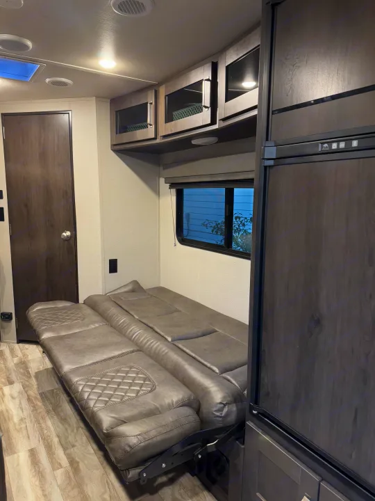 RV rental: The interior features a versatile gray fold-out sofa bed, dark refrigerator, and overhead cabinets with a window.. Grand Design Transcend Xplor 2021