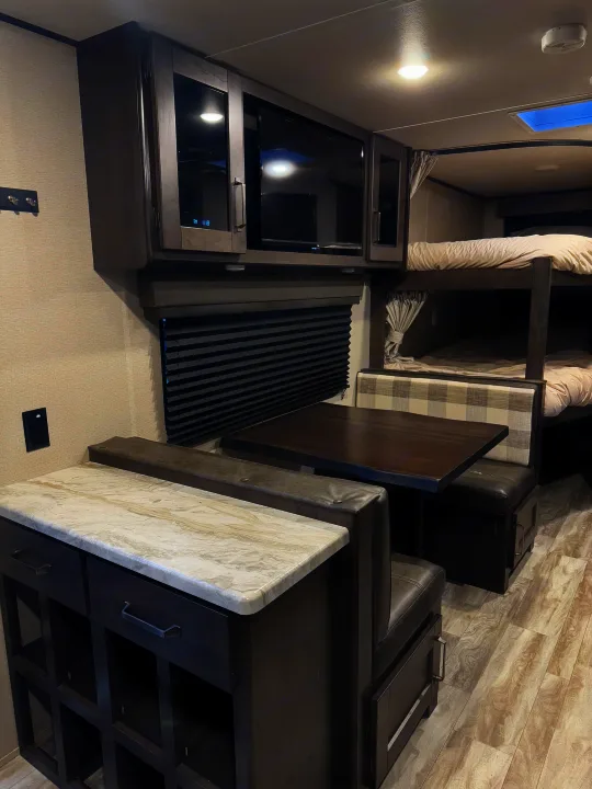 Comfortable RV rental interior showcasing a dinette, kitchen counter, and cozy bunk beds. Ideal for family adventures.. Grand Design Transcend Xplor 2021