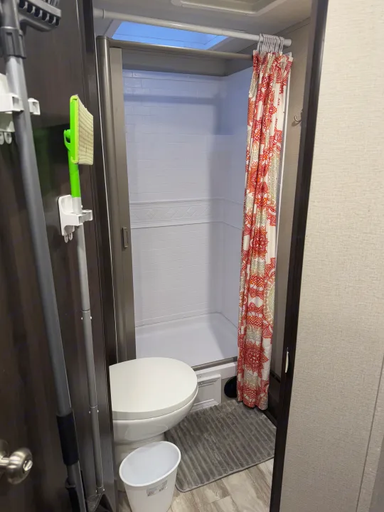 Compact RV rental bathroom with shower, toilet, and storage for cleaning tools. Features a decorative shower curtain and skylight.. Grand Design Transcend Xplor 2021
