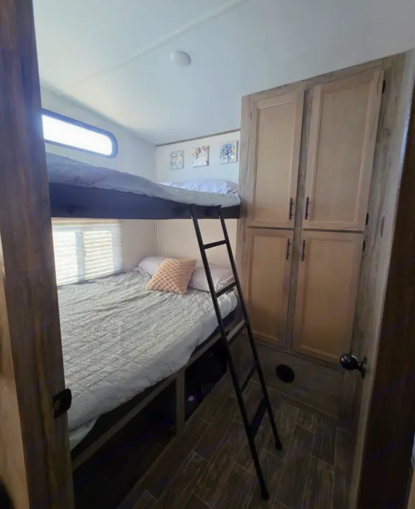 Cozy RV rental interior features comfortable bunk beds with a ladder, window blinds, & storage cabinets. Ideal for family camping.. Forest River Cherokee Arctic Wolf 2021