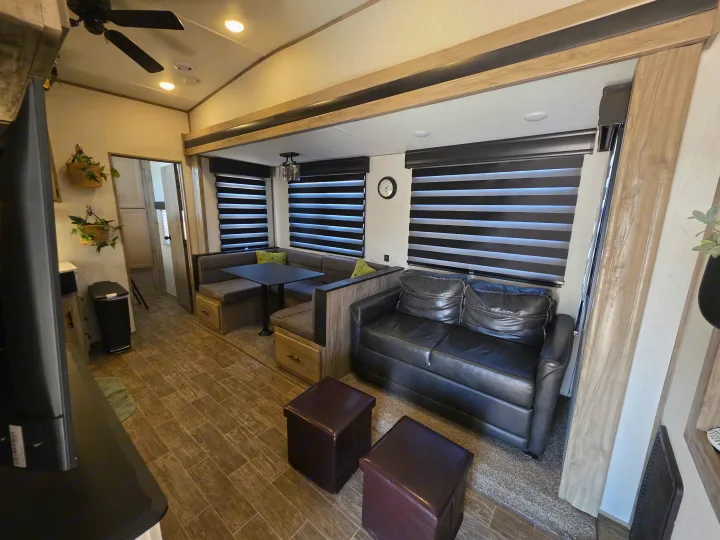 Inside an RV rental: a modern living area with dinette booth, dark sofa, and wood-look flooring, designed for comfort.. Forest River Cherokee Arctic Wolf 2021