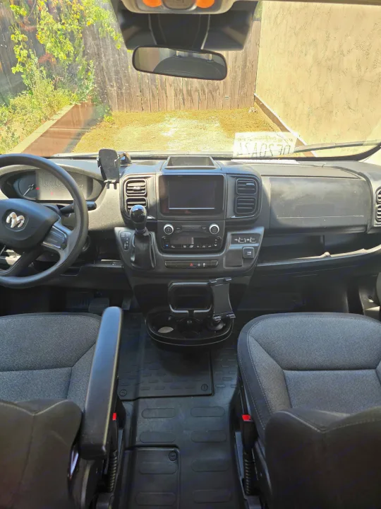 Interior of an RV rental van's front cabin, showing the dashboard, Ram steering wheel, seats, and backyard view.. Ram Promaster 2022
