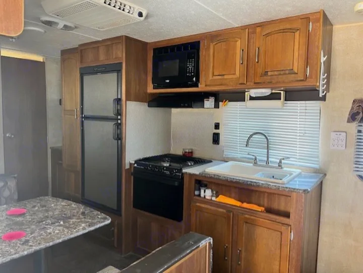 RV rental interior: full kitchen with refrigerator, microwave, stove, sink, and dining area, featuring wood cabinets.. Keystone RV Summerland 2015