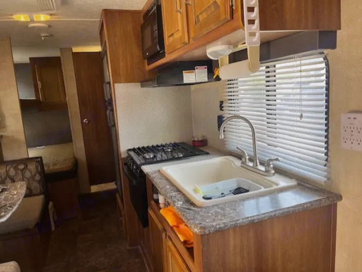 This RV rental shows a compact kitchen with sink, stove, & microwave. Dinette & sleeping area are also visible.. Keystone RV Summerland 2015