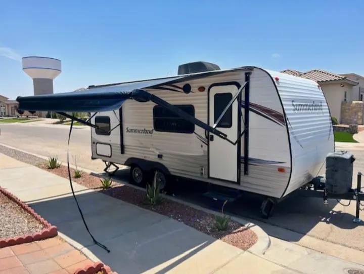 A white Summerland travel trailer RV rental with its awning extended, parked on a street in a sunny residential area.. Keystone RV Summerland 2015