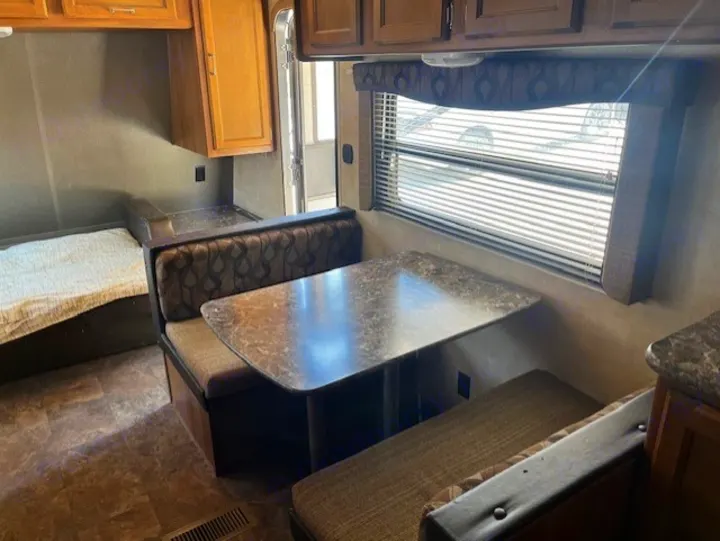 View inside an RV rental showing a functional dinette, built-in bed, & storage cabinets for travel.. Keystone RV Summerland 2015