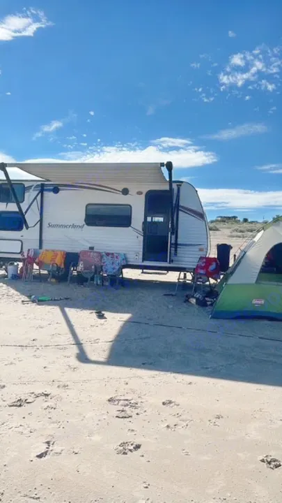 An RV rental travel trailer and green tent create a cozy campsite on a sunny, sandy beach under a blue sky.. Keystone RV Summerland 2015