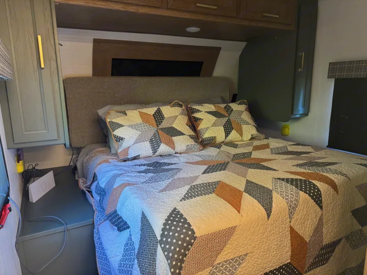 Cozy RV rental bedroom features a patterned quilt, headboard, and compact storage for a comfortable travel experience.. Heartland RVs Eddie Bauer 2024