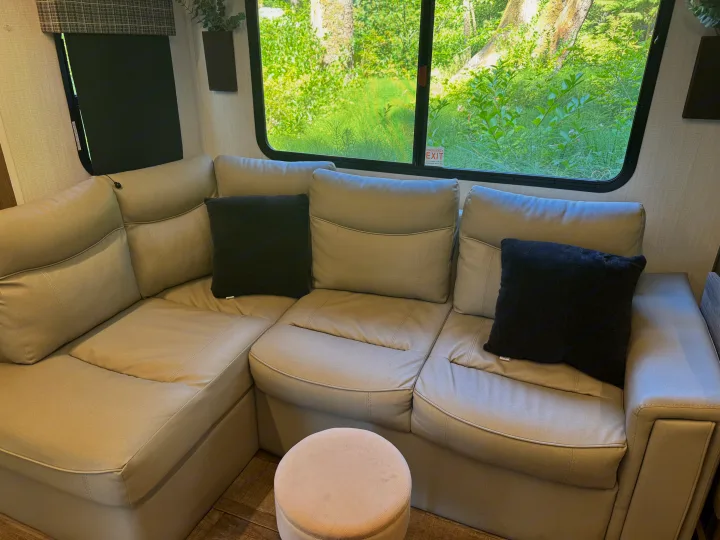 Relax in this RV rental's comfy living area, featuring a light sectional sofa, dark pillows, and nature view window.. Heartland RVs Eddie Bauer 2024