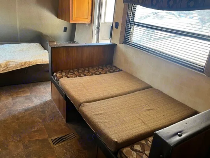 Spacious RV rental interior featuring a convertible dinette seating area, cozy bed, and large window for comfortable travel.. Keystone RV Summerland 2015