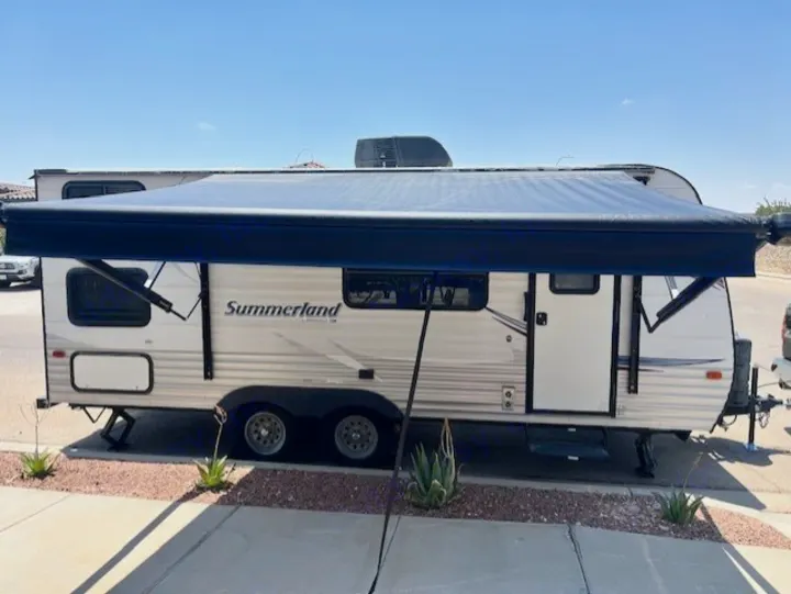 Travel trailer RV rental with large blue awning extended, parked outdoors. Perfect for your next shaded adventure or camping trip.. Keystone RV Summerland 2015