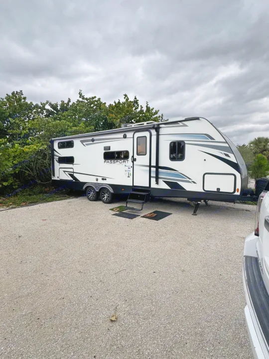 White travel trailer RV rental parked on a gravel campsite under a cloudy sky, ready for your outdoor escape.. Keystone RV Passport TT 2022