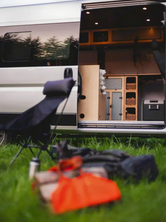 RV rental with custom interior revealed through open door. Camping chair & gear on grass highlight outdoor comfort.. Wayfarer Walt 2021