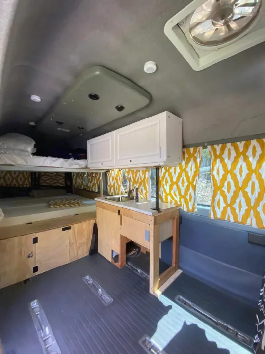 Cozy RV rental camper van interior with bunk beds, compact kitchen, and bright curtains.. Dodge Sprinter 2006