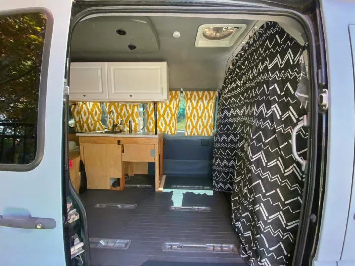 Inside this cozy RV rental: a modern van conversion with a kitchenette, bright yellow window curtains, and a patterned privacy curtain.. Dodge Sprinter 2006