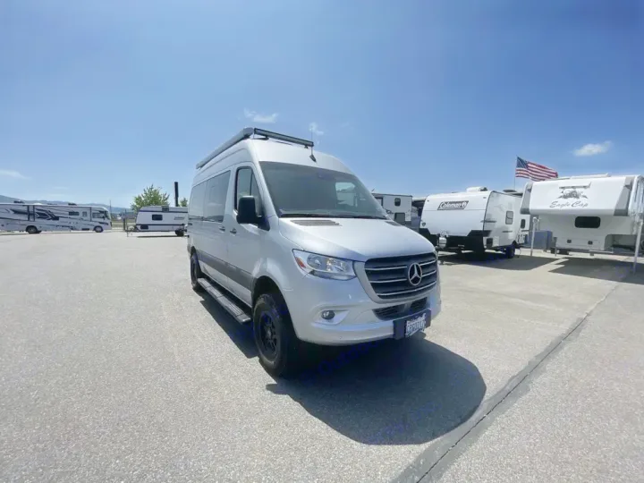A silver Mercedes-Benz Sprinter van, an ideal RV rental, parked in a sunny outdoor lot with other RVs under a clear sky.. Thor Tranquility 2022