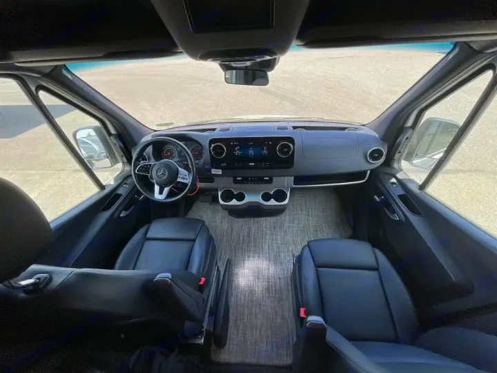 Inside an RV rental: front cockpit view with a black steering wheel, modern dashboard, and two leather seats.. Thor Tranquility 2022