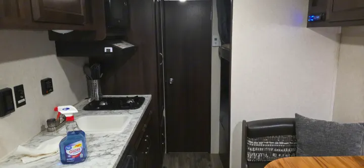 Inside a clean RV rental: kitchen with stove, sink, and cleaner, next to a bunk bed area and dining space.. Jayco Jay Flight SLX 2018
