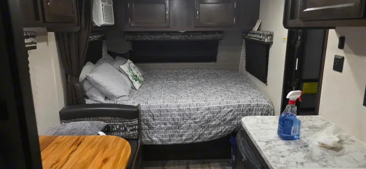 Experience an RV rental's cozy interior, featuring a compact bedroom with a patterned bed, overhead cabinets, and a small side counter.. Jayco Jay Flight SLX 2018