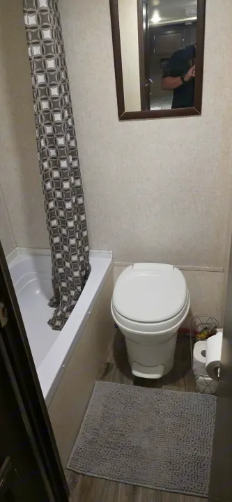 RV rental bathroom showcasing a tub-shower, compact toilet, mirror, and grey patterned shower curtain.. Jayco Jay Flight SLX 2018