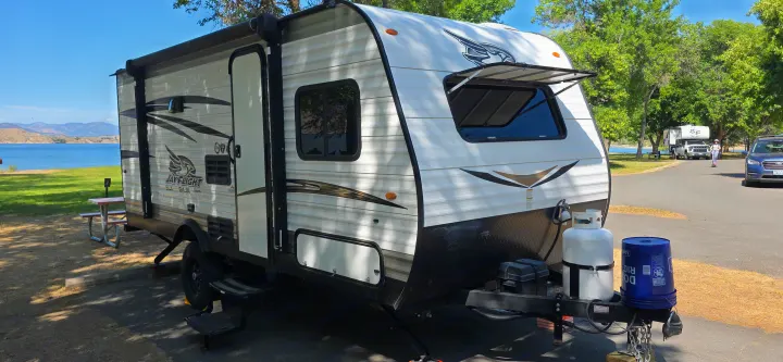 RV rental at a scenic lakeside campsite. This white travel trailer offers outdoor adventure and comfortable camping by the water.. Jayco Jay Flight SLX 2018
