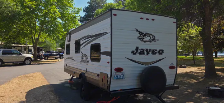 Jayco travel trailer as an rv rental parked at a serene Washington campground, surrounded by lush trees and other vehicles.. Jayco Jay Flight SLX 2018